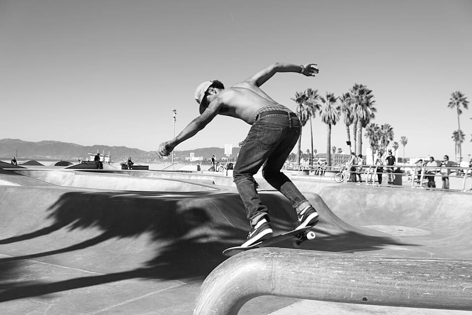 A skateboarder dropping into a bowl at a busy outdoor skate park