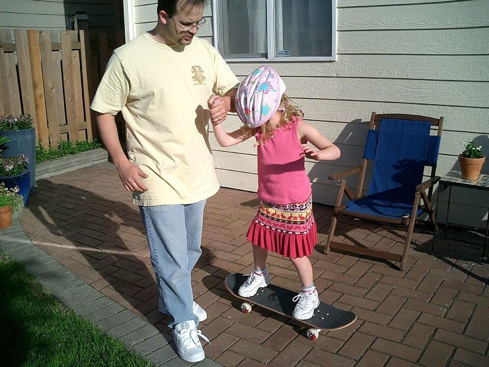 A parent helping a young child in a helmet balance on a skateboard